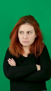 Kizil saçli bir kiz kollarini göğsünün uzerinde birlestiriyor, beline sariliyor, tatsiz bir sekilde yan tarafa bakiyor. Olumsuz duygular. Kızıl saçlı, yeşil arka planda, krom anahtarlı genç bir kadın. 