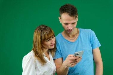 Sorunları çözmek için internette telefon araması yapan bir adam yeşil arka plan kromatonlu bir kadına mavi tişörtlü beyaz ceketli doğada insanların dokunmatik haber kaynaklarını aydınlatmasında yardımcı olur. aygıt.