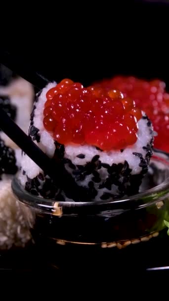 赤いキャビア サーモン マグロ キュウリ アボカドを黒い背景に隔離したウラマキ寿司のクローズアップ 寿司ロールで美味しい和食 赤と黒のキャビアと寿司 — ストック動画