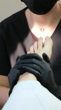 Profesyonel ayak masajı, pedikür salonunda ayak bakımı yapan siyah eldivenli kadın doktor ve maske, dairesel yoğurma hareketleriyle masaj yapıyor ayak tedavisi sorunları. pedikür salonu