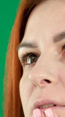 Heyecan deneyimlemenin heyecanı. Pembe saçlı kız elleriyle dudaklarına dokunuyor. Kızıl saçlı genç kadın yeşil arka planda. Krom anahtar duygular. 