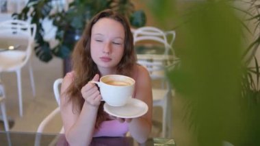 Avrupalı genç bir kadın kafede çikolatalı süt içiyor. Pembe elbiseli genç bir kız bir restoranda büyük bir kupa kapuçino lattesinden çay içer. Sokak kafesinde cappuccino içiyorduk. 4k görüntü
