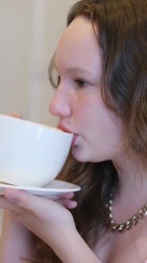 Avrupalı genç bir kadın kafede çikolatalı süt içiyor. Pembe elbiseli genç bir kız bir restoranda büyük bir kupa kapuçino lattesinden çay içer. Sokak kafesinde cappuccino içiyorduk. 4k görüntü