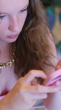 Pembe elbiseli bir kız telefonla mesaj yazmaya odaklanmış, telefon aletine bağımlı, akıllı telefonla zaman geçiriyor. Yüksek kalite 4k görüntü