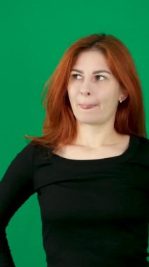 Kız düşünceli bir şekilde somurttu, sonra parlak bir şekilde gülümsedi. Bir şey buldum, dikey video. Kızıl saçlı, yeşil arka planda genç bir kadın. Krom anahtar duygular, yakın çekim kahverengi gözler. 