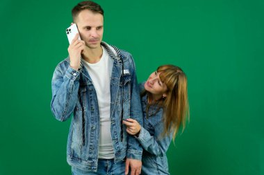 Cheerful guy and girl in denim clothes, couple, family. guy calling on the phone, Girl eavesdropping on a conversation, on a green background. High quality photo clipart
