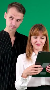 Siyah beyaz elbiseli bir adam ve bir kız, Yin-Yang, yeşil arka planda bir tablete bak, konuş ve gülümse, dikey video. Yüksek kalite 4k görüntü