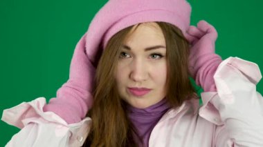 Pembe eldivenli ve pembe bereli güzel, şık bir Fransız kadın beresini düzeltiyor, gülümsüyor ve çerçeveye bakıyor. Yeşil bir arka planda. Yüksek kalite 4k görüntü