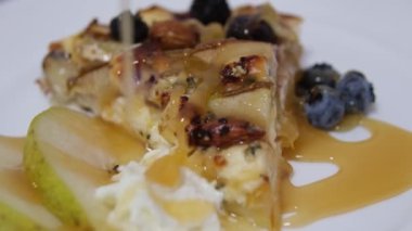 Turta, çeşitli peynir aperatifleri ve çam fıstıklı taze armutlar, bal serpilmiş. Lezzetli ve sağlıklı, beyaz tabakta dönüyor, yavaş çekim, yüksek kalite 4K görüntü.