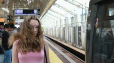 Vancouver 'da bir kız hava trenini bekliyor, tren yaklaşıyor, arabalar geçiyor, saçları gelişiyor, pembe elbisesi genç bir Kanadalı. Yüksek kalite 4k görüntü
