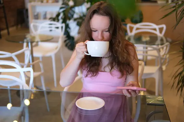Pembe elbiseli genç bir kız bir kafede cappuccino içerken bir restoranda büyük bir bardak cappuccino latte içiyor. Avrupalı genç bir kadın kafede çikolatalı süt içiyor. Yüksek kalite