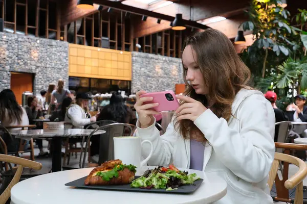 Yemek, aşçılık, teknoloji ve insan konsepti. Akıllı telefonlu kadın elleri restoranda jambonlu salatayı taştan tabakta fotoğraflıyor. Yüksek kalite fotoğraf