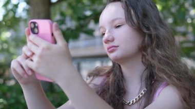 Yakın plan güzel bir kız pembe bir telefonla oynar, bir numarayı çevirir, internetten alır, sosyal ağlarda yazışır. Açık havada, yüksek kalitede 4K görüntü.