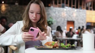 Genç bir kız yemek yer, yemek yer ve telefonu kullanır. Çalışma, mola, kafe, restoran, öğle yemeği. Yüksek kalite 4k görüntü