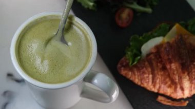 Lokantanın lezzetli içeceği sütlü sağlıklı yeşil çay. Peynirli ve salatalı kruvasan yemek, Fransız kahvaltısı, öğle yemeği, atıştırmalık, akşam yemeği, diyet, lezzetli. Yüksek kalite 4k görüntü