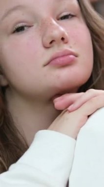 Kafede oturan beyaz elbiseli genç bir kız kameraya hava öpücüğü yolluyor. Dikey video, 