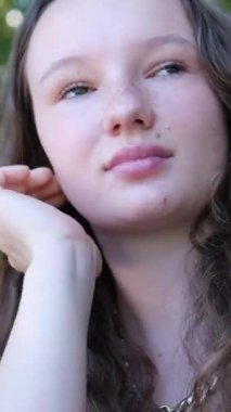 Dalgın genç bir kız, açık havada, kıvırcık saçlarını düzeltiyor. Dikey videolar, yüksek kalite 4k görüntü