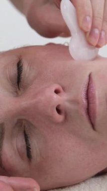 Yüz masajı için gua sha kazıyıcı ile yüz masajı, profesyonel yanak masajı, güzellik salonu, gençlik uzaması, yüz sağlığı. Dikey video
