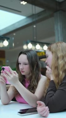 İki mutlu genç kadın kapalı kafede akıllı telefondan sosyal medyada geziniyor. Teknoloji, yaşam tarzı, arkadaşlık ve insanlar. İki kızın kafe telefonu.