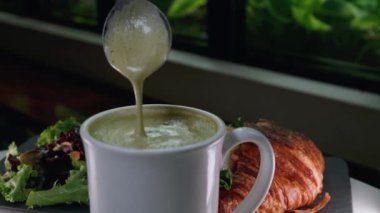 Matcha latte 'nin üstündeki köpüğü çıkartırken en üstteki görüntü. Taze kruvasanla servis edilen sağlıklı sütsüz içecek. Yüksek kalite 4k görüntü