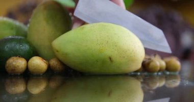 Cam bir masada, yeşil mangoyu parçalara ayır. Kadın eli, mangonun nasıl kesildiğini gösterir. Yüksek kaliteli FullHD görüntüler