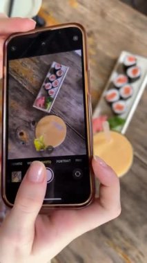 Bir kız yemek bloğunu yönetmek için cep telefonuyla suşi ve mango suyu çekiyor, bir blogcu bir restoranda çalışıyor ve yemek yiyor, yemeklerini filme alıyor ve fotoğraf çekiyor. Yemek fotoğrafları çekiyor.