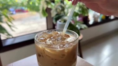 Bir kadının eli buzlu latte içerken, tropik bir ülkede buzlu kahve içerken, pipetle içerken, pipetten sıvı çekerken. Yüksek kalite 4k görüntü