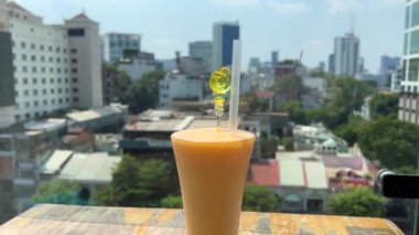 Güneşli bir günde, uzun bir bardağa doldurulmuş taze mango suyunun yakın plan görüntüsü. Ho Chi Minh şehrinin arka planında bir restoranda