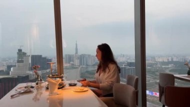 Şık bir restoranda çay partisi, genç bir kız pastayla çay içiyor ve Ho Chi Minh City Vietnam 'da panoramik bir pencerenin yanında birkaç video çekiyor. Restoran panoramik vitrininde bir kız