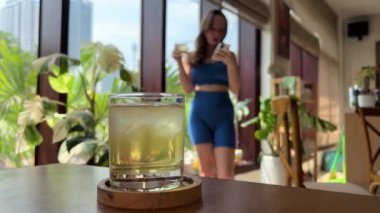 Sporcu kız eğitimden sonra pencerenin yanında buzlu çay içer, sağlıklı beslenme konsepti. sağlıklı bir hayat. Yüksek kalite 4k görüntü