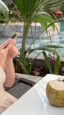 Bir kız canlı yayın yapıyor, sosyal ağlar için bir blok çekiyor ve bir video yayınlıyor. Tropikal bir ülkede Hindistan cevizi içmek