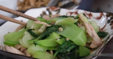 Ahşap çubuklarla Bakmi Çin eriştesi topluyorum. Kapatın. Yemek çubuğuyla sebze ve et ye.