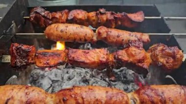 Lezzetli sıcak kebap. Şiş kebap ve ızgarada kızarmış sosis. Sosis ve et şişlerini ızgaradan çıkar. Et ızgaradaki sıcak kömürlerde pişiriliyor, pişirmek için şişler üzerinde dönüyor.. 