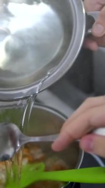 Çorbaya su ekle Aşçı fırında patates, havuç ve soğan dolu bir kaba bir bardak su dök, mutfakta aşçı pişir. Omuz manzarası üzerinden.