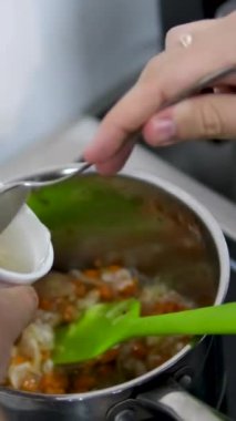 Aşçı fırında patates, havuç ve soğan dolu büyük bir saksıya bir bardak su dolduruyor. Mutfakta aşçı omuz manzarası üzerinden yemek pişiriyor. Köri çorbasına pirinç ekle.