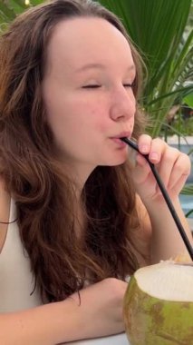 Havuz başında rahatlayan, hindistancevizi içen, lüks tatiller yapan genç bir kadın. Kız kokteyl ile saman kullanıyor. Özel havuz alanı, satılık villa. Elit gayrimenkul alımı. 