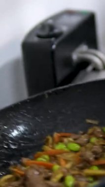 Asya restoranının mutfağında aktif olarak çalışan yakın plan şef karışık renkli sebzeler yavaş çekimde tavada kızartılıyor. Sebzeleri kızartma tavasına at.
