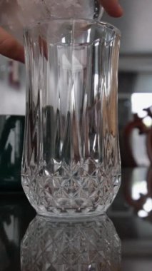 Buz tabakasının yavaş çekim görüntüsünde buz tüpünü masanın üzerindeki bardağa dökerken doğal bir arka plan, düşük açı ve yörünge dönüş kamerası görüntüsü..