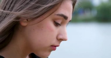 Bir nehrin arka planında genç bir kızın yüzü, aşağı inmiş, cep telefonuna bakıyor, haberleri okuyor, aletlere doğadan daha fazla zaman harcıyor, aletlere bağımlı. 4k 