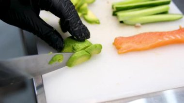 Kadın şef suşi yapar ve pirinç, kırmızı balık ve avokadodan rulo yapar. Yakından yemek pişirir. Suşi hazırlama süreci Master sınıfı. Adım adım Video seti