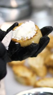 Sandviç krem peynirli sandviçe yayılmış. Siyah eldivenli eller ekmeğin üzerine kızarmış ekmek döker.