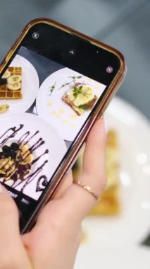 Yukarıdan bir kadın bir kafede akıllı telefondan tatlı fırlatıyor. Bir sosyal ağa yüklemek için kahvaltısını filme alıyor. Çikolata ve böğürtlenli Belçika waffle 'ı.