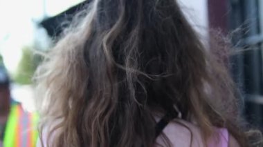 Sokakta yürüyen kız saçlarını düzleştiriyor, arkadan görünüşü, ağır çekim. Yüksek kalite 4k görüntü