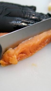 Somon parçalarını siyah eldivenli büyük bir bıçakla kesin mutfakta beyaz bir tahtanın üzerinde pişirin. Yüksek kalite 4k görüntü