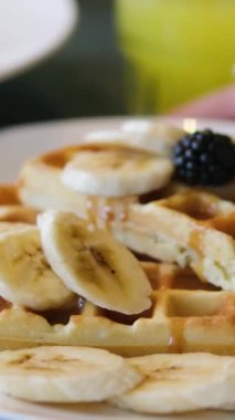 Yukardan çilek soslu ve kremalı tatlı waffle renkli masa arkasında pembe tepside hafif mutfakta sıcak süt içeceği ile servis edilir. Kahvaltıda waffle.. 