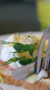 Sağlıklı sabah yemeği. Otelde kahvaltıda nefis haşlanmış yumurta yiyen bir adam. Erkek eli Benedict yumurtasının içinde yumurta sarısı, hollandaise sosu ve İngiliz çöreğinde ıspanak var.. 