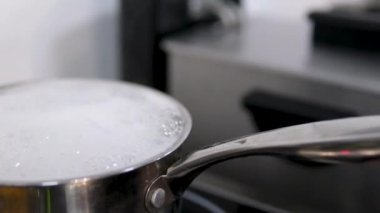 Kırsal ocakta haşlanan tencere ve sıvı su dışarı akıyor yanık ve kapağı çıkarıyor. Statik yakın çekim. Su kaynıyor ve köpük akıyor.