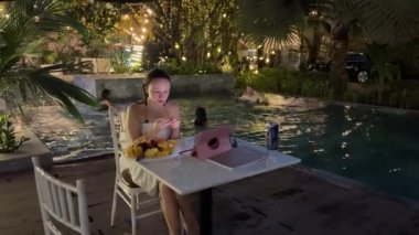 Havuz kenarındaki kız internette meyve yemeyi öğreniyor. Arka planda çocuklar su sıçratan gençlerle oynuyor. Ho Chi Minh Şehri Vietnam 09.05.2024