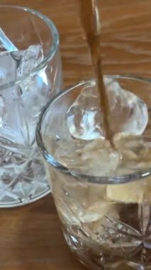 Kola bir bardağa doluyor, bir sıçrama yaratıyor ve bir damla kenardan aşağı akıyor, ahşap kahverengi bir masada parlak bir gölge, yan görüş masaya kola dökülüyor. Yüksek kalite 4k görüntü