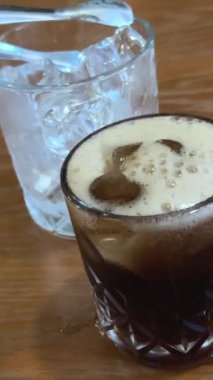 Yakın plan, bardağa içki dolduruyor. Kız cam bardağa döküyor. Kafede. Karbonatlı koyu içecek dökün.